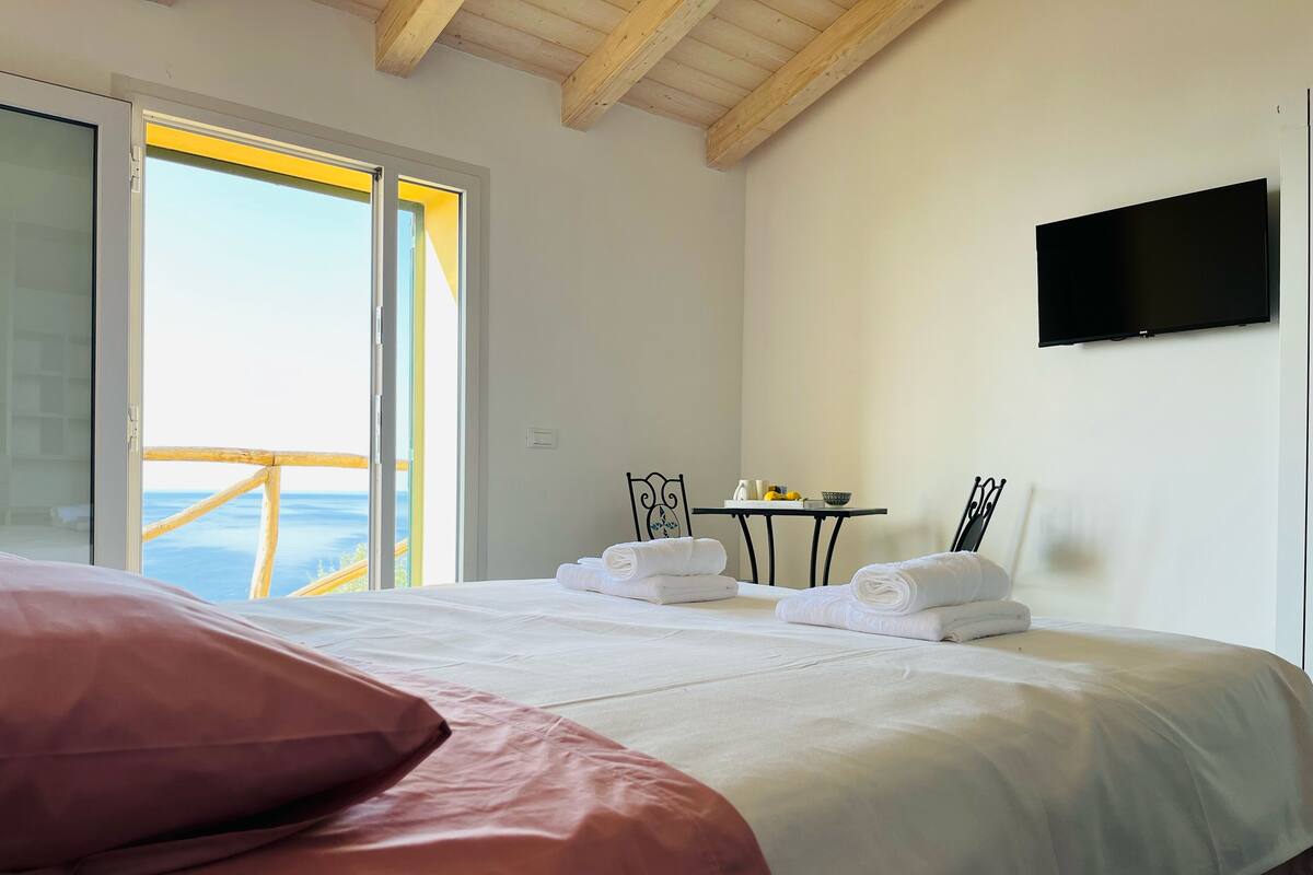 A hotel room with a bed, a table with towels, a TV, and a balcony with a view.