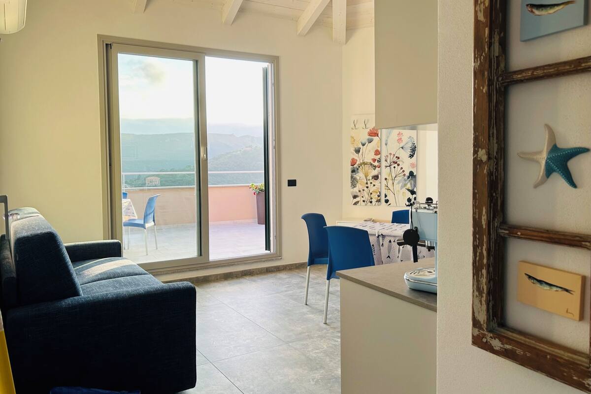 A room with a balcony, a dining area, and a kitchen.