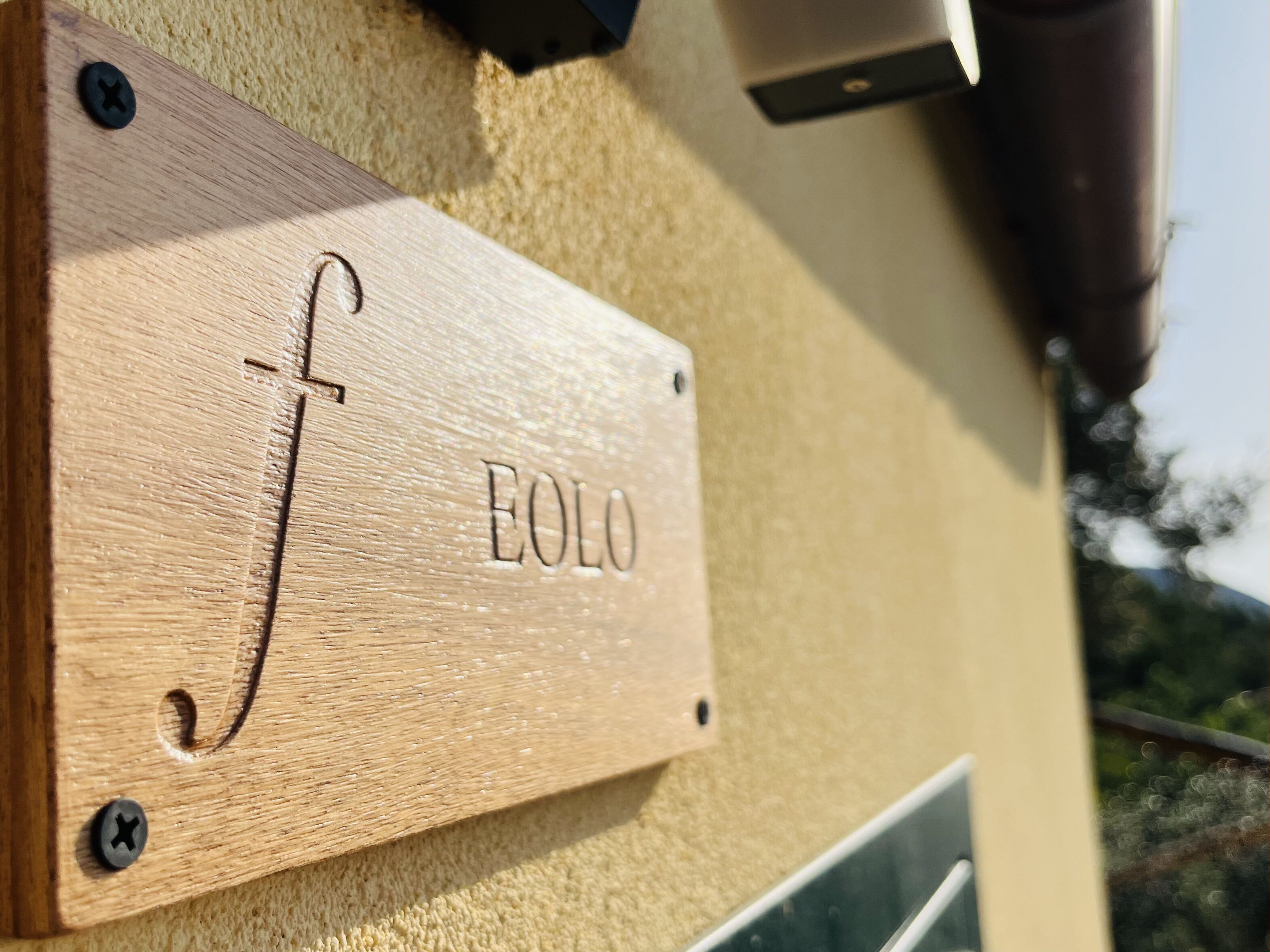 A wooden plaque with the name "Eolo" mounted on a textured wall.