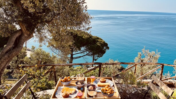 A wooden table with a tray of food and drinks, overlooking a coastal view. - Eufonia del Mare (Finale Ligure)