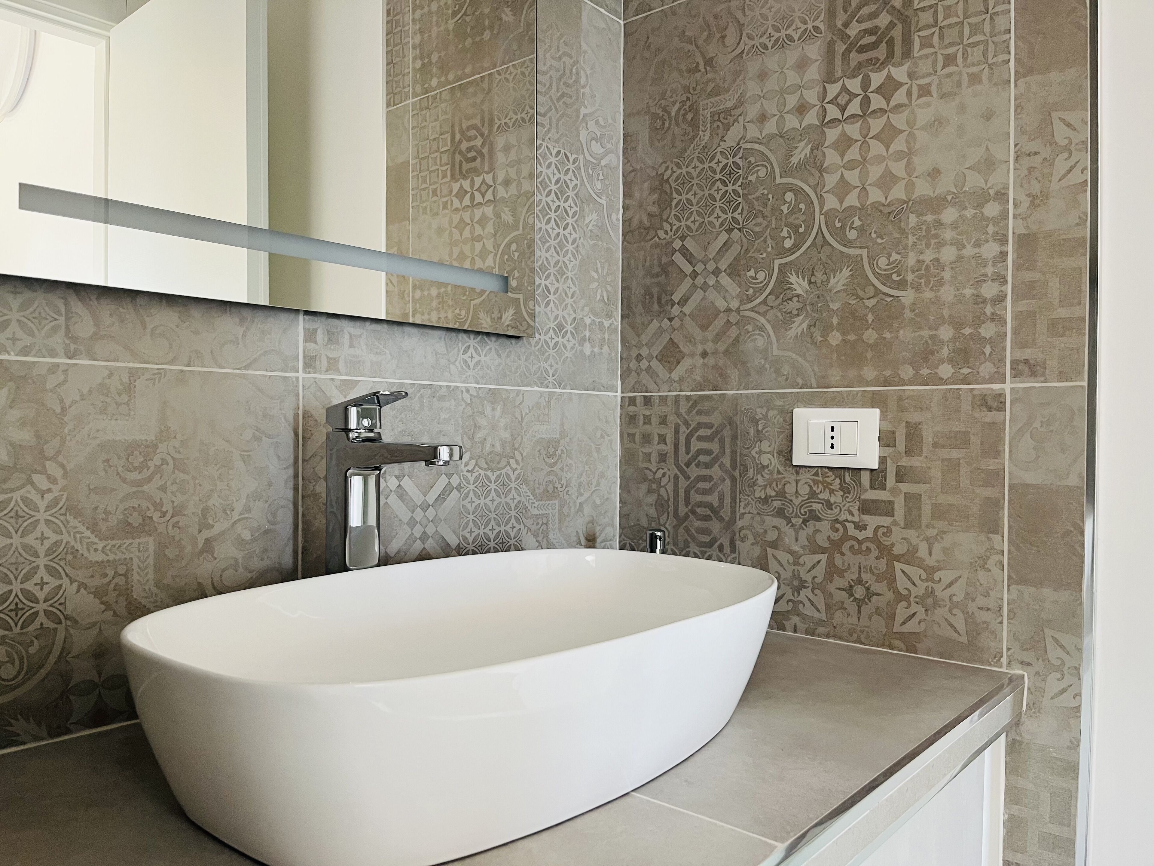 A bathroom with a white oval sink, a chrome faucet, and patterned tiles on the walls.