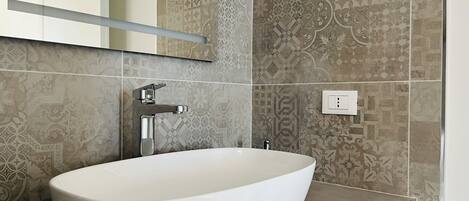 A bathroom with a white oval sink, a chrome faucet, and patterned tiles on the walls.