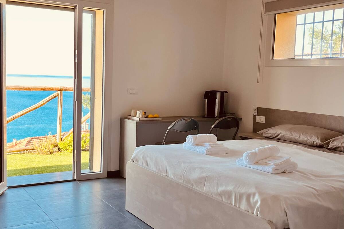 A hotel room with a bed, a desk, a coffee machine, and a view of the sea.
