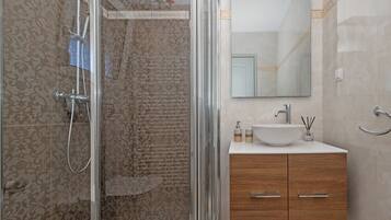A bathroom with a glass shower enclosure, a sink with a mirror, and wooden cabinets.