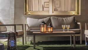 Un coin salon accueillant avec un canapé, une petite table, deux lanternes allumées et deux verres posés sur la table.