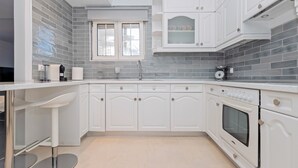 Une cuisine moderne avec des meubles blancs, un four encastré et une fenêtre au-dessus de l’évier.