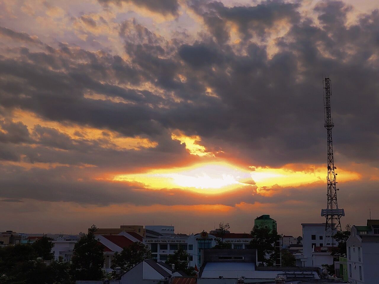 A cityscape at sunset with buildings and a communication tower.