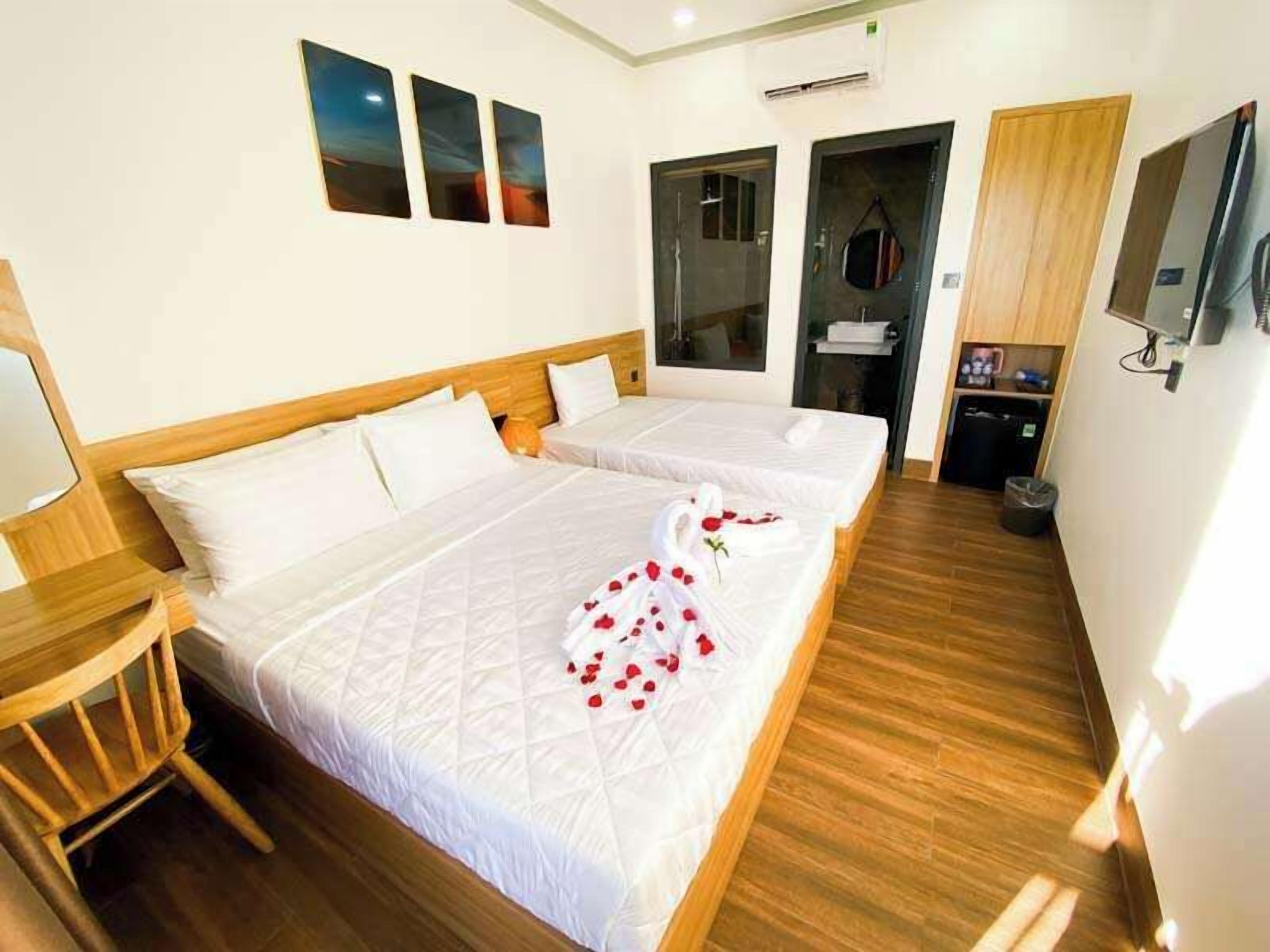 A hotel room with two beds, a wooden floor, a TV, and a shower area.