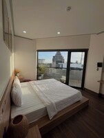 Un dormitorio moderno con una cama grande, vistas a un edificio a través de una puerta de cristal y una mesita de noche con un florero.