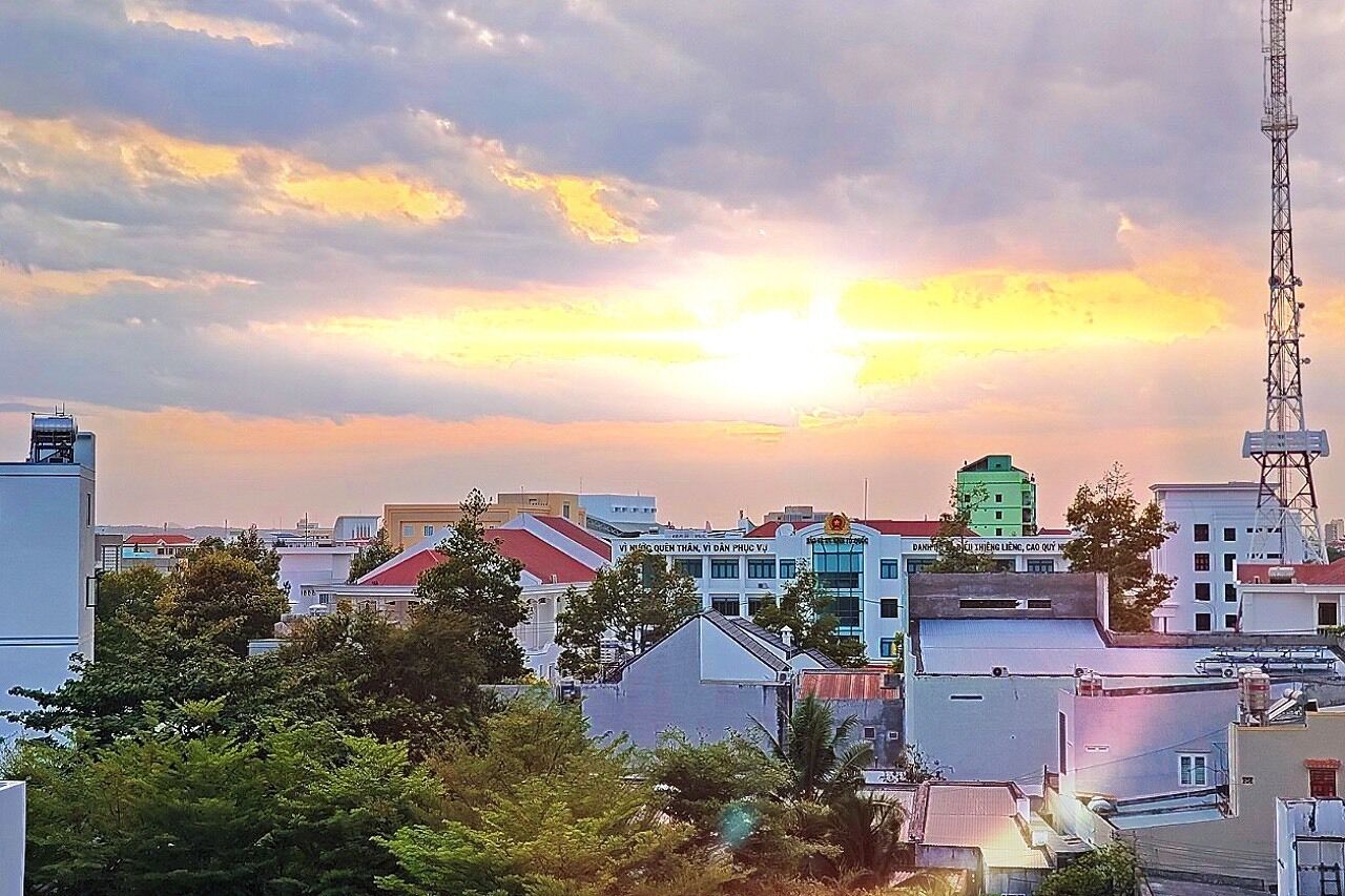 A cityscape at sunset with buildings, a water tower, and a communication tower.