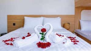 A neatly made bed with white linens, a decorative swan made of towels, and red rose petals and roses.
