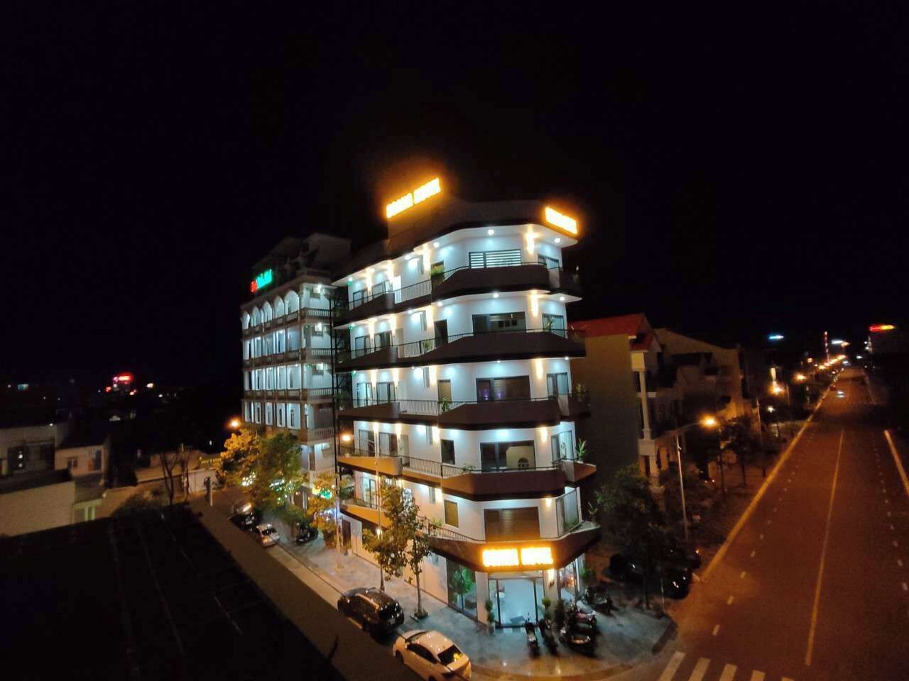 A multi-story hotel with illuminated signage, a street in front, and parked cars.