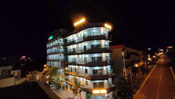 A multi-story hotel with illuminated signage, a street in front, and parked cars.