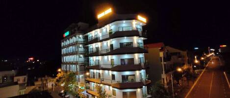 A multi-story hotel with illuminated signage, a street in front, and parked cars.