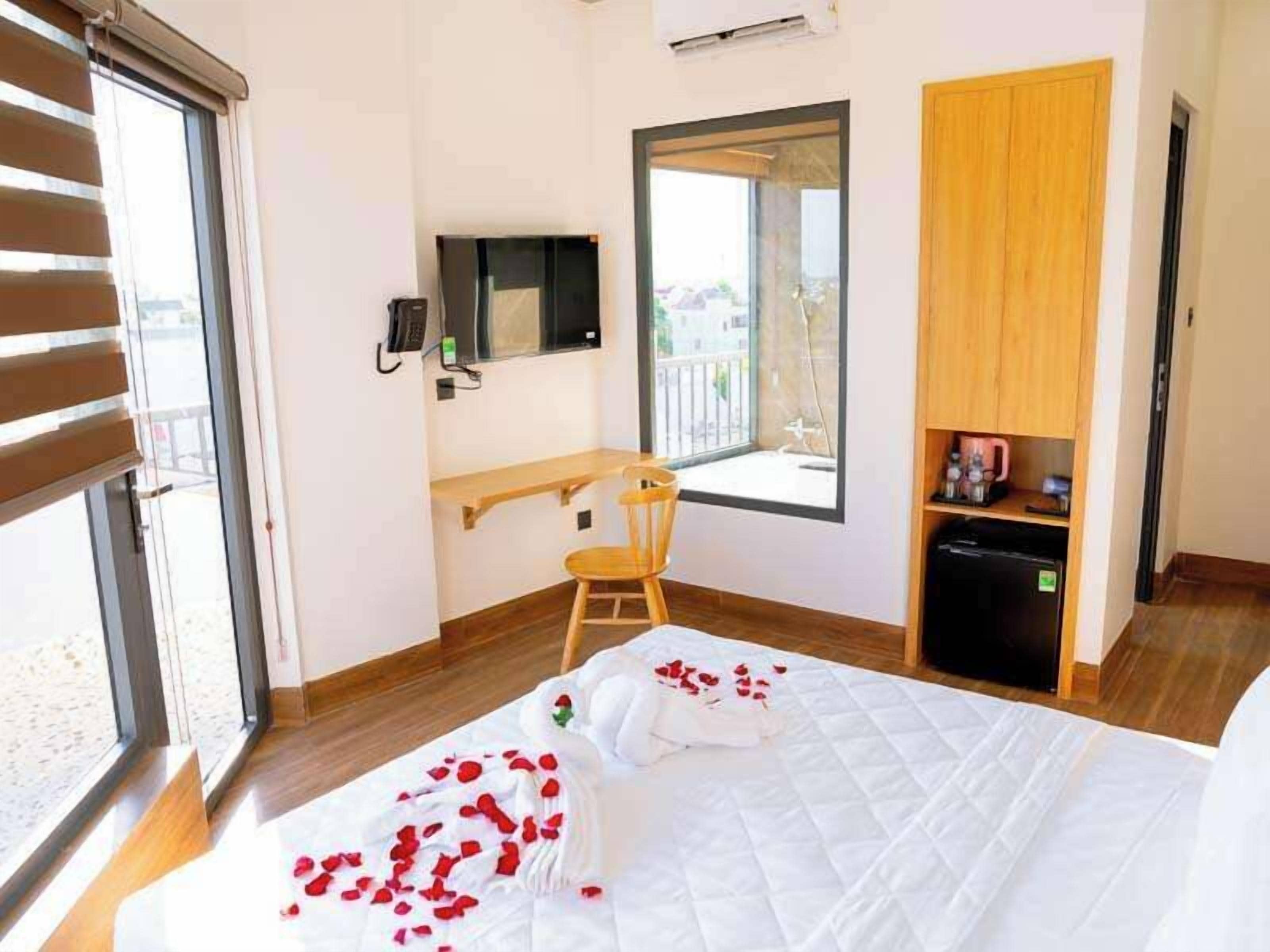 Een hotelkamer met een bed, een bureau, een stoel, een kleine kitchenette en een groot raam.