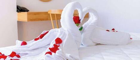 Una cama con sábanas blancas y dos toallas con forma de cisne adornadas con pétalos de rosa roja.