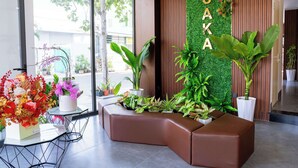 A reception area with a curved brown seating area, a green wall with the name 'OSAKA', and various potted plants.