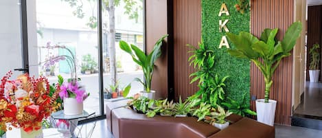 Un área de recepción con una zona de estar marrón curva, una pared verde con el nombre 'OSAKA' y diversas plantas en macetas.