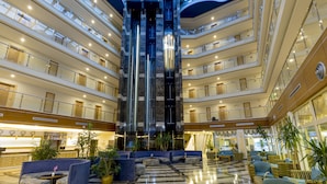 A multi-level hotel lobby with a central elevator, seating areas, and a marble floor. - Holiday Garden Resort - All inclusive (Alanya)