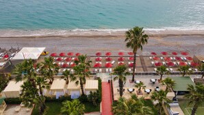 An aerial view of a beachside resort with rows of red umbrellas, white lounge chairs, and palm trees. - Holiday Garden Resort - All inclusive (Alanya)