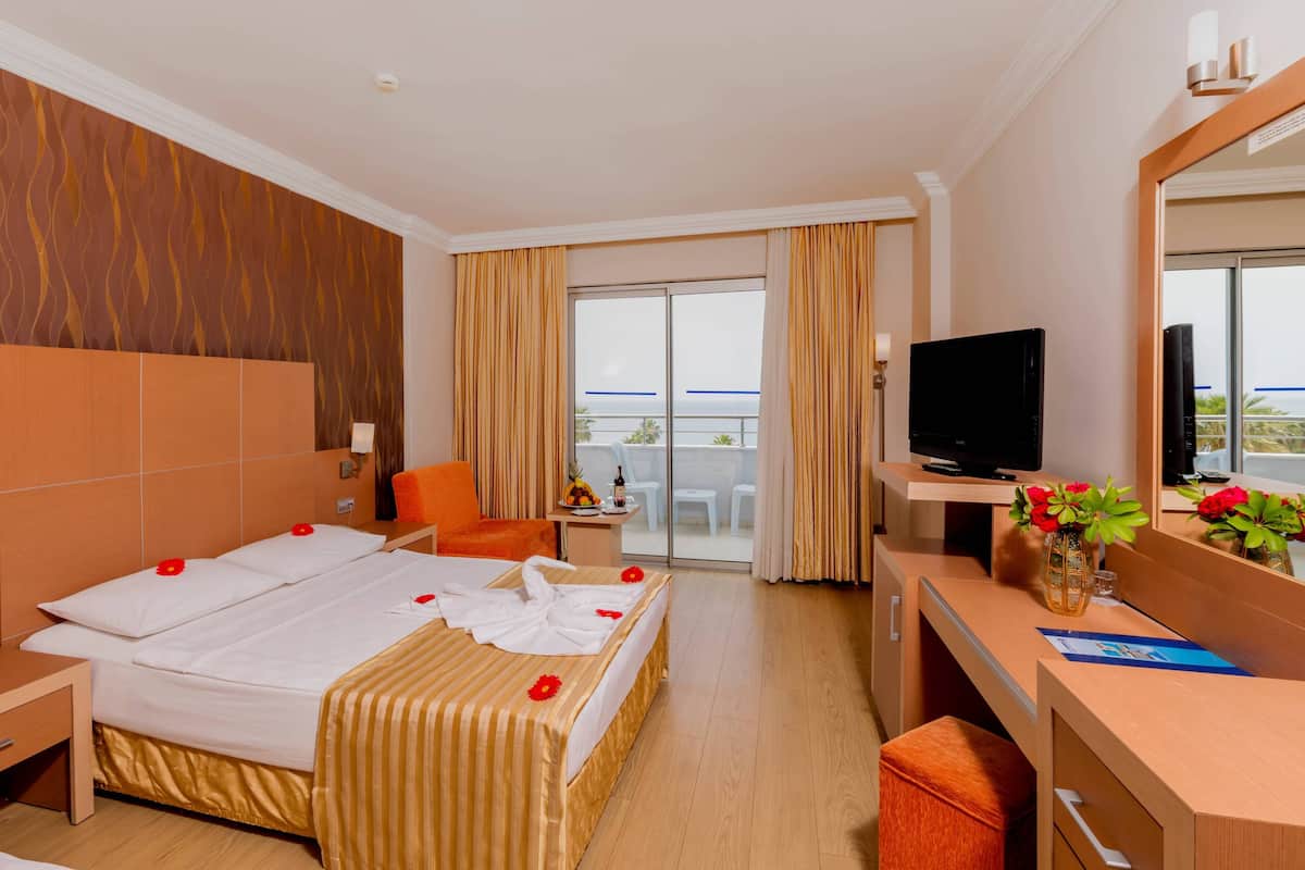 Ein Hotelzimmer mit Bett, Schreibtisch, Fernseher und einem Balkon mit Vorhängen.