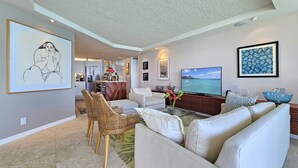 A modern living room with a large flat-screen TV, comfortable seating, and artwork on the walls. - RELAX w/ Direct Beach Access High Flr. Sans Souci 2BD/2BA🌴Stunning Ocean Views  (Honolulu)