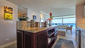 A modern kitchen with granite countertops, a built-in oven, and a dining area with a view of the ocean. - RELAX w/ Direct Beach Access High Flr. Sans Souci 2BD/2BA🌴Stunning Ocean Views  (Honolulu)