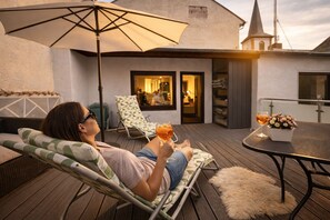 A person relaxing on a lounge chair with a drink, a table with a flower vase, and a view of a building with a tower. - 170 qm2 Großes, Gemütliches Haus mit Kamin und Klimaanlage. Hunde Erwünscht! (Kestert)