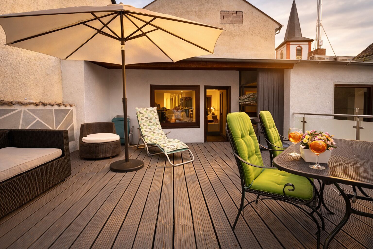 A wooden deck with outdoor furniture, including a sofa, two lounge chairs, and a table with drinks and flowers.