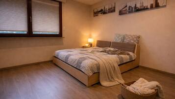 A bedroom with a bed, a window with blinds, a lamp, and a wall with cityscape artwork.