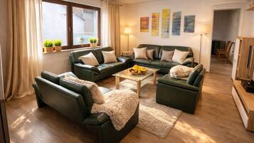 Ein modernes Wohnzimmer mit einer Sofagarnitur, einem Couchtisch mit Früchten und Blick ins Freie durch ein Fenster.