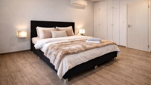 A modern bedroom with a black bed frame, white bedding, a fur throw, and a nightstand with a lamp. - 170 qm2 Großes, Gemütliches Haus mit Kamin und Klimaanlage. Hunde Erwünscht! (Kestert)
