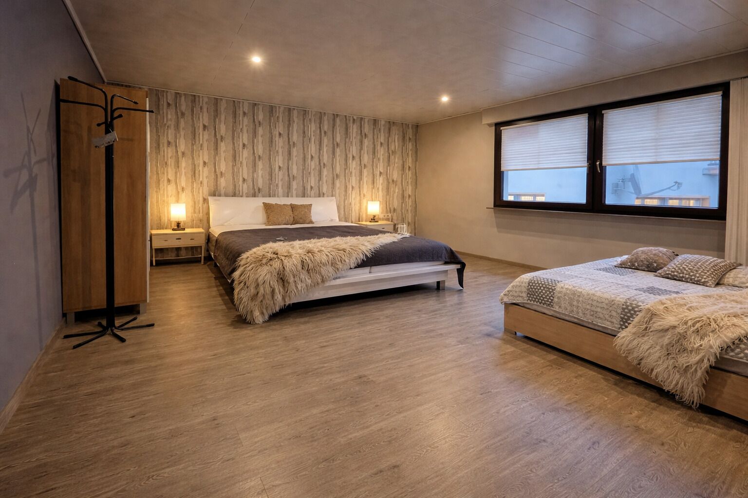 A bedroom with a large bed, a smaller bed, a wardrobe, a nightstand, and a window with blinds.
