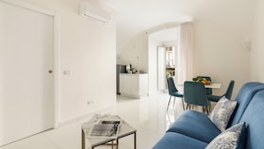 Una sala de estar moderna con un sofá azul, una mesa de centro de vidrio y vistas a la cocina y el comedor.