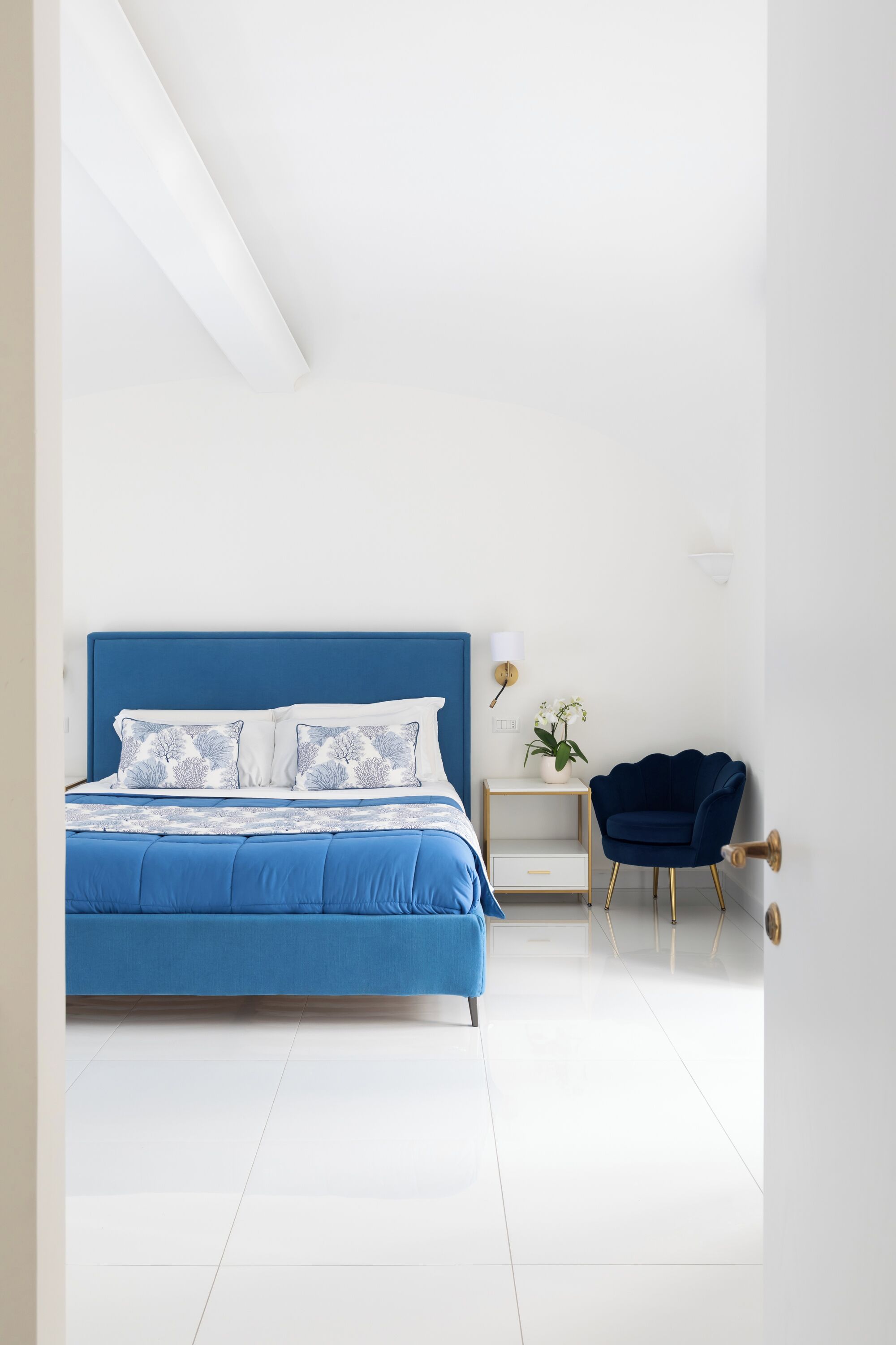 Ein Schlafzimmer mit einem blauen Bett, weißen Wänden und einem kleinen Beistelltisch mit einer Pflanze.