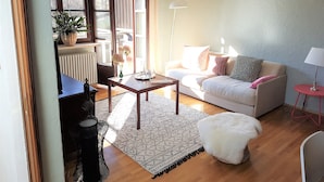 A living room with a sofa, coffee table, and a lamp. There is a window with curtains and a plant on the windowsill. - Gemütliche Whg. mit Balkon und Bergblick im Oberallgäu! Ruhig und Zentrumsnah (Immenstadt im Allgäu)