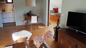 A modern living room with a wooden floor, a TV, a dining area with a table and chairs, and a kitchen visible in the background. - Gemütliche Whg. mit Balkon und Bergblick im Oberallgäu! Ruhig und Zentrumsnah (Immenstadt im Allgäu)