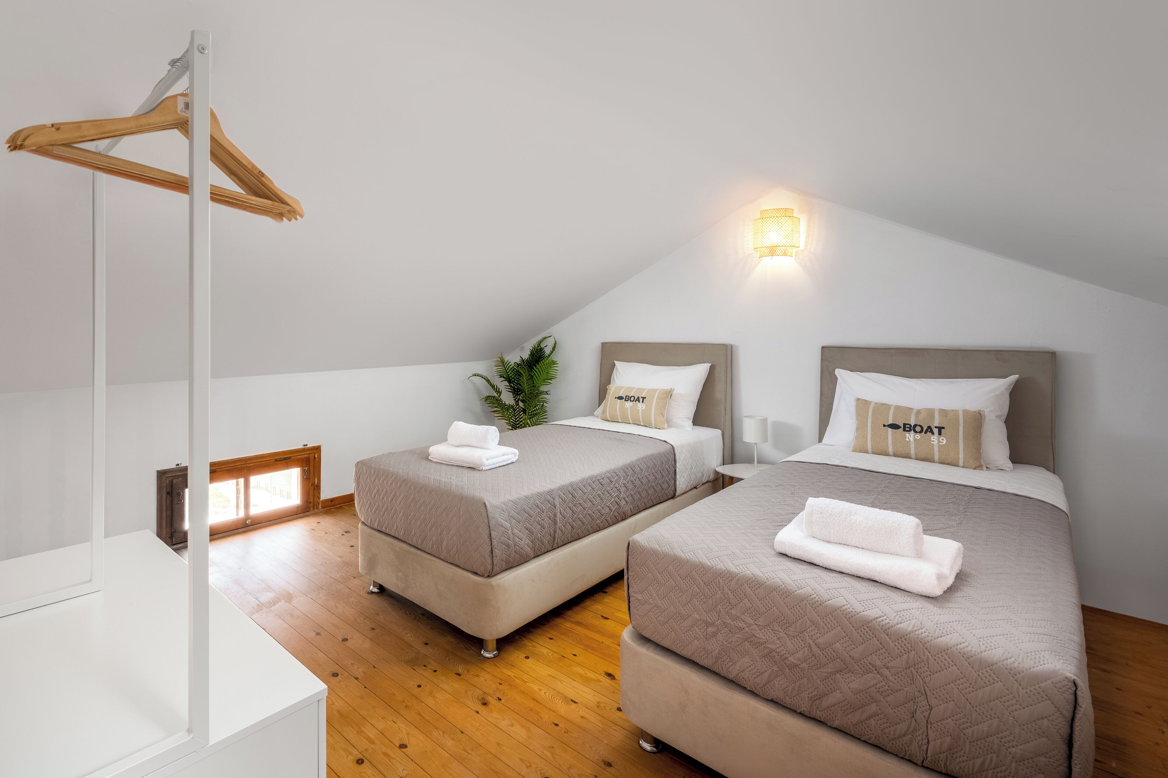 Ein Schlafzimmer mit zwei Betten, einem Holzgalgen, einer Pflanze und einer Wandleuchte.