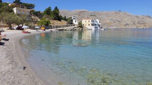 A coastal area with clear waters, a pebble beach, and buildings on a hillside. - Villa in Symi, with sea view (simi)