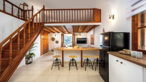 A kitchen with a wooden staircase, a central island with stools, a refrigerator, and a TV. - Villa in Symi, with sea view (simi)