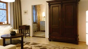 A room with a large wooden wardrobe, a round table with a vase, and a chair. There is a door leading to another room.