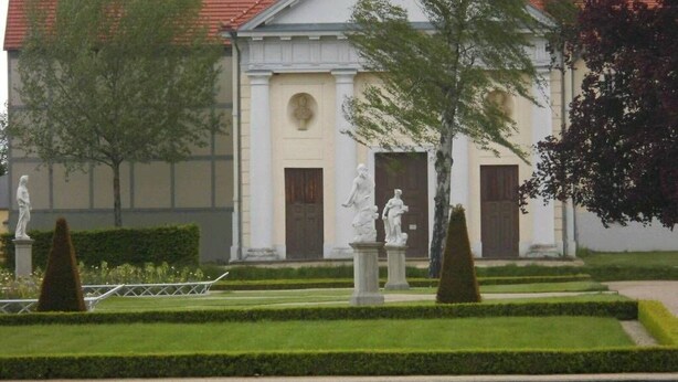 A building with classical architecture, a manicured garden, and statues.