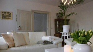 Una sala de estar con un sofá blanco, una mesa de centro, una planta en maceta y un jarrón con flores.