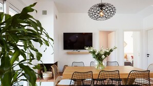 A dining area with a wooden table, black wire chairs, a black TV on the wall, and a potted plant.