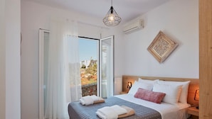 A bedroom with a bed, a nightstand, a wall-mounted lamp, a window with curtains, and a view of the outside.