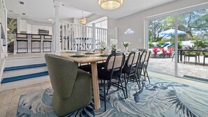 A modern kitchen with white cabinets, a dining area with a wooden table and chairs, and a view of the outdoor patio. - Pickleball Paradise - Heated Pool-Hot Tub-Game Room (Tampa)