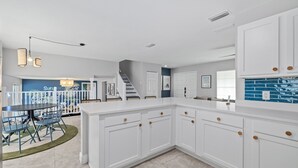 A spacious kitchen with white cabinetry, a dining area with blue chairs, and a staircase leading to another level. - Pickleball Paradise - Heated Pool-Hot Tub-Game Room (Tampa)