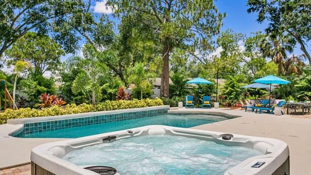 A hot tub surrounded by a swimming pool, lounge chairs, and umbrellas in a landscaped outdoor area. - Pickleball Paradise - Heated Pool-Hot Tub-Game Room (Tampa)