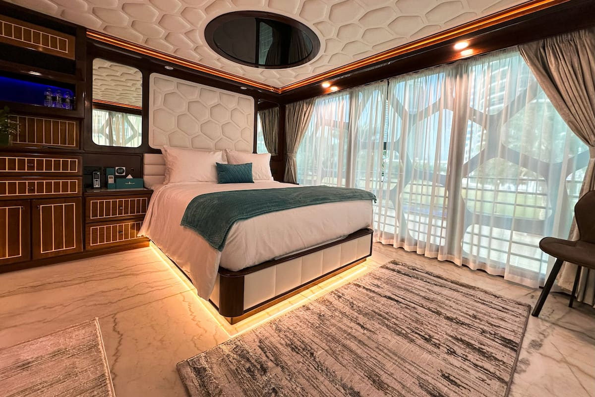 A modern bedroom with a large bed, a built-in TV, and a large window with curtains.
