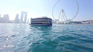 Un traversier transportant des passagers, une grande roue et des bâtiments modernes en arrière-plan.